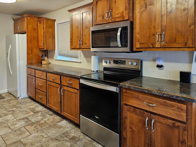 kitchen featuring brown cabinetry, decorative backsplash, stone finish floor, dark stone countertops, and stainless steel appliances