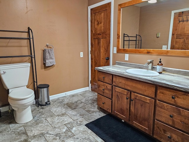 bathroom with baseboards, stone finish flooring, toilet, and vanity