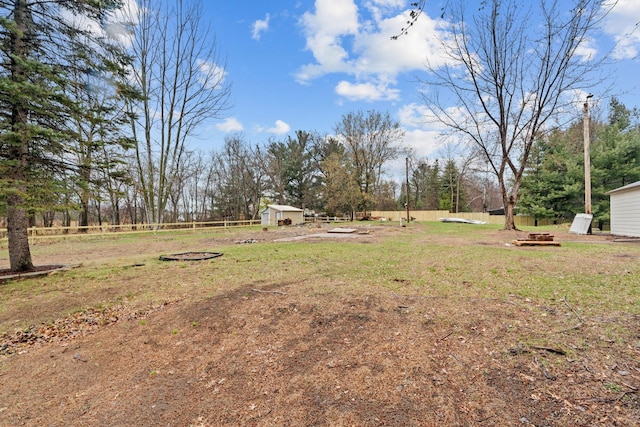 view of yard with a storage unit, fence, an outbuilding, and a fire pit