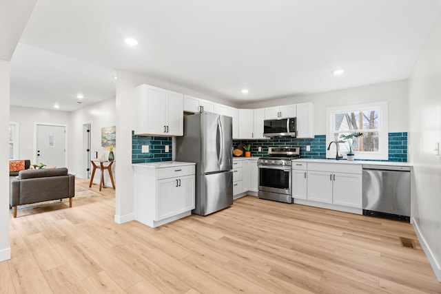 kitchen with appliances with stainless steel finishes, decorative backsplash, light countertops, light wood-style floors, and recessed lighting