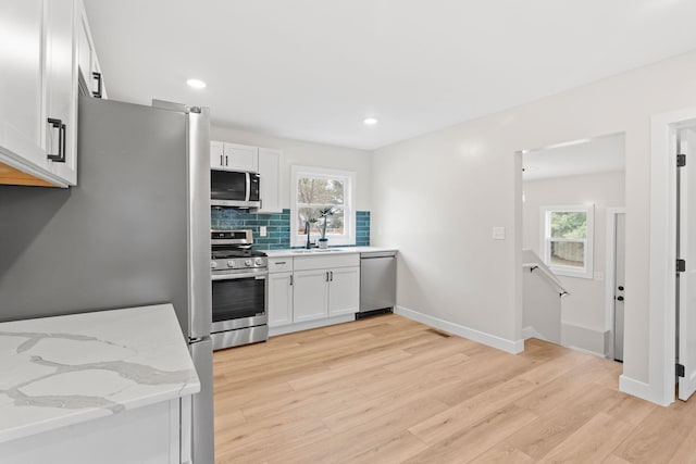 kitchen with stainless steel appliances, a sink, light wood-type flooring, tasteful backsplash, and healthy amount of natural light