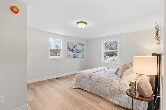 bedroom with multiple windows, light wood-style flooring, and baseboards