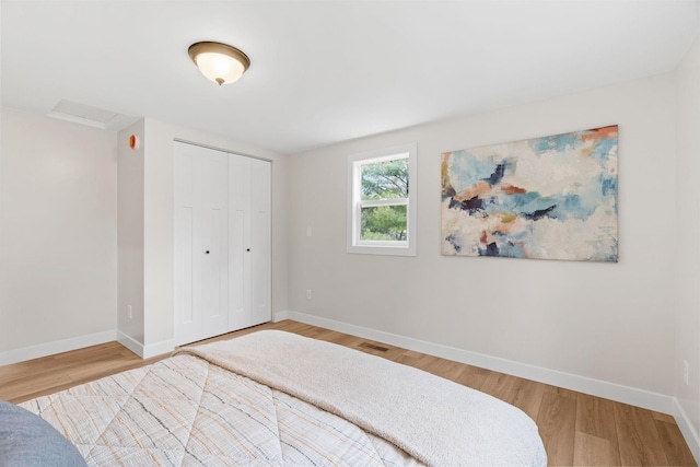 bedroom with baseboards, wood finished floors, a closet, and attic access