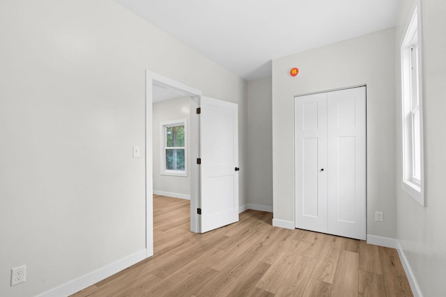 unfurnished bedroom featuring light wood-type flooring, baseboards, and a closet
