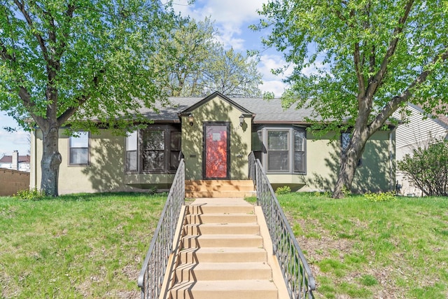 view of front of property featuring roof with shingles, stucco siding, and a front yard