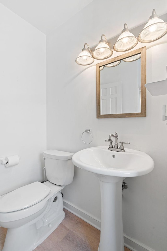 half bath featuring baseboards, wood finished floors, and toilet