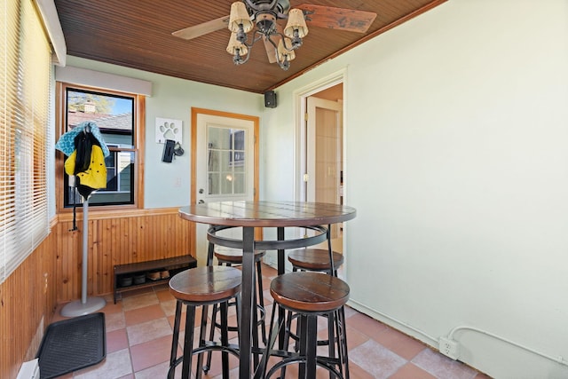dining space featuring wooden walls, a wainscoted wall, and a ceiling fan