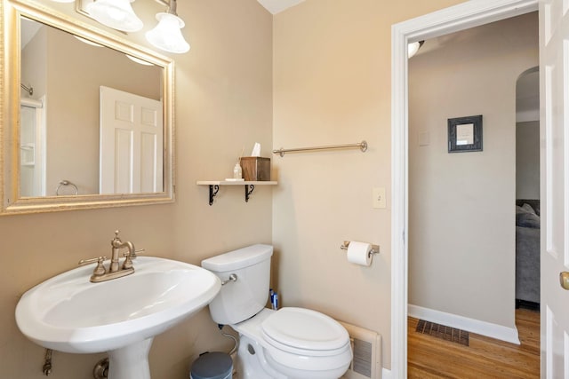 half bath featuring a sink, toilet, baseboards, wood finished floors, and visible vents