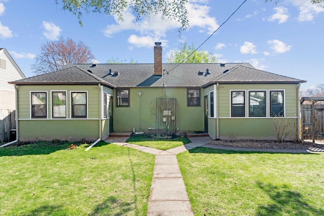 exterior space with a chimney, roof with shingles, a lawn, fence, and stucco siding