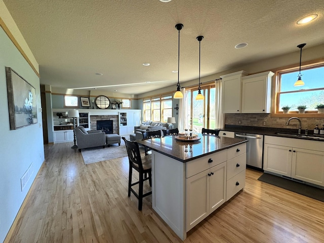 kitchen featuring stainless steel dishwasher, dark countertops, light wood-type flooring, a textured ceiling, and a sink