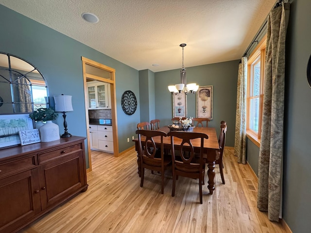 dining room with an inviting chandelier, a textured ceiling, light wood-style flooring, and baseboards