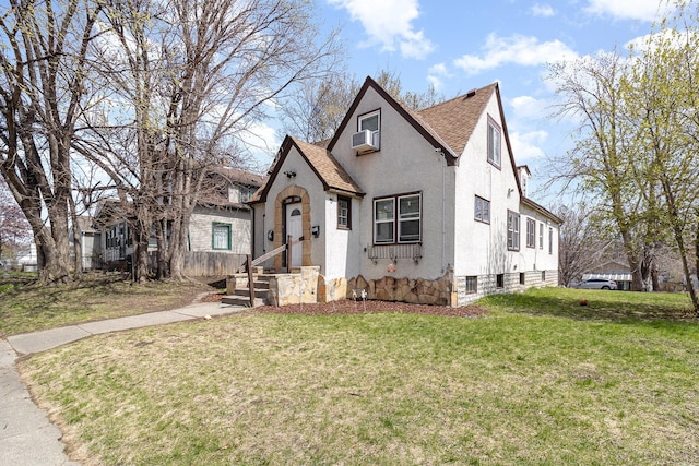 english style home with a front lawn, a shingled roof, and stucco siding