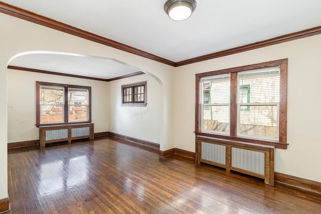 spare room featuring radiator heating unit, wood finished floors, baseboards, and arched walkways