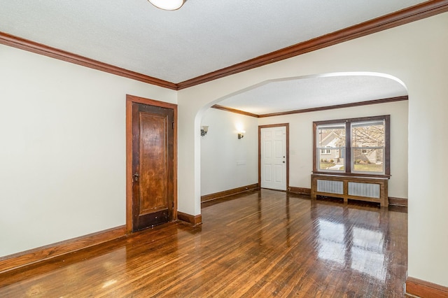 empty room featuring radiator, baseboards, ornamental molding, arched walkways, and hardwood / wood-style floors