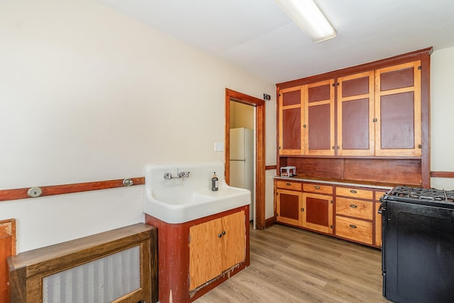 kitchen featuring light wood finished floors, brown cabinets, black range with gas stovetop, glass insert cabinets, and freestanding refrigerator