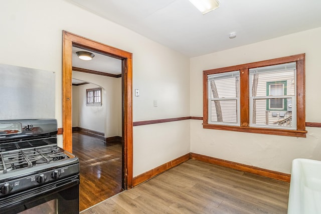 interior space with gas stove, arched walkways, wood finished floors, and baseboards