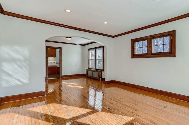 empty room featuring hardwood / wood-style floors, baseboards, crown molding, and arched walkways