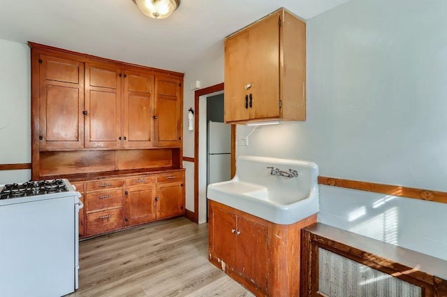 kitchen with light wood-type flooring, white appliances, and brown cabinets