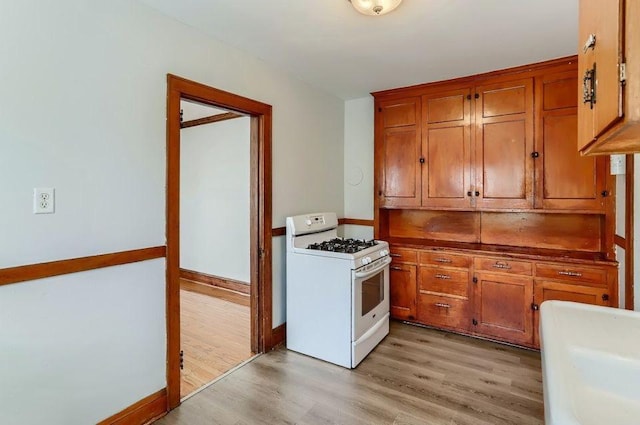kitchen with white gas range oven, light wood-type flooring, brown cabinetry, and baseboards