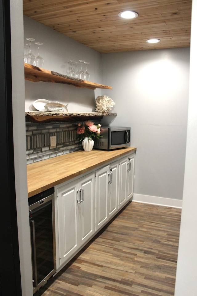 indoor dry bar featuring wine cooler, stainless steel microwave, baseboards, wood finished floors, and wood ceiling