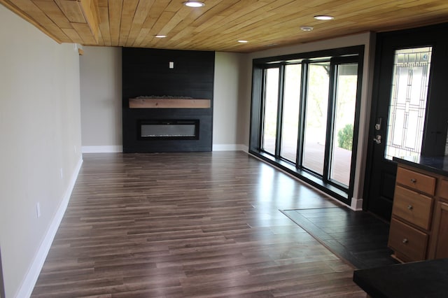 unfurnished living room featuring recessed lighting, a glass covered fireplace, baseboards, wood ceiling, and dark wood-type flooring