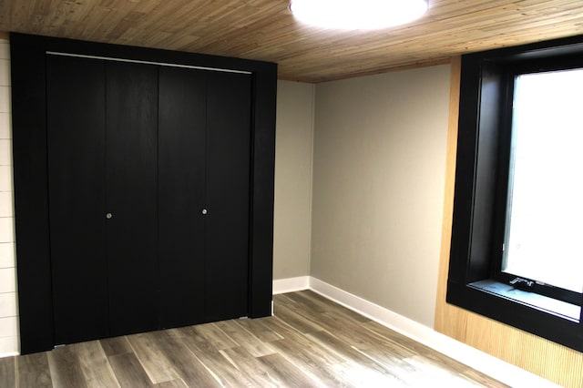 unfurnished bedroom with wood ceiling, baseboards, wood finished floors, multiple windows, and a closet