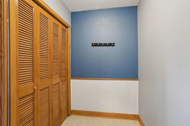 hallway featuring a textured ceiling, baseboards, and wainscoting