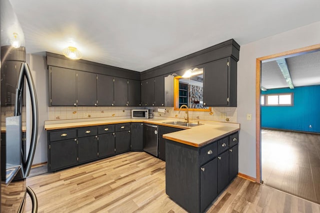 kitchen featuring a sink, stainless steel appliances, light wood-type flooring, backsplash, and light countertops