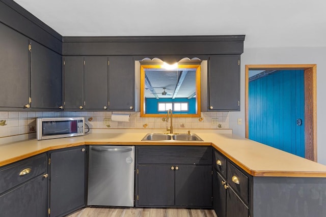 kitchen with a sink, a peninsula, decorative backsplash, light countertops, and appliances with stainless steel finishes