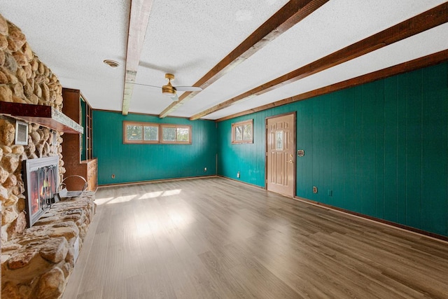 unfurnished living room with a textured ceiling, ceiling fan, wood finished floors, a fireplace, and beam ceiling