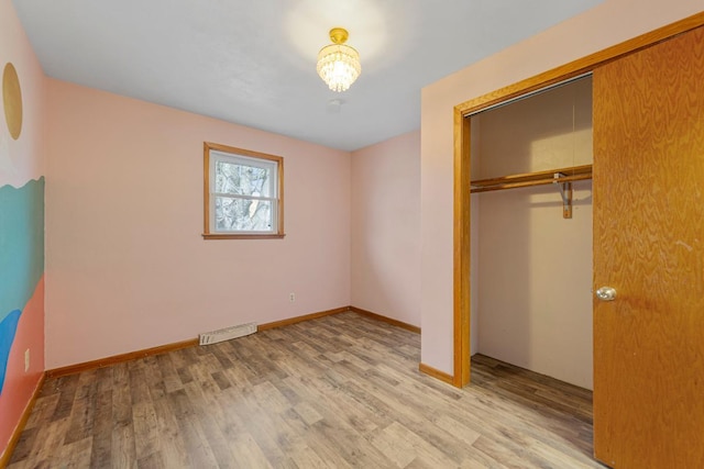 unfurnished bedroom with baseboards, a closet, visible vents, and wood finished floors