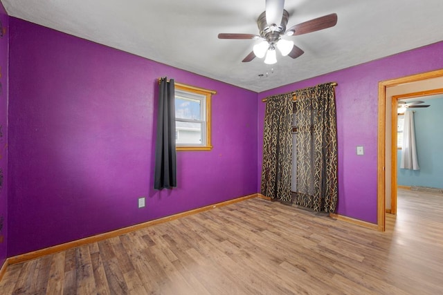 unfurnished room with baseboards, wood finished floors, and a ceiling fan