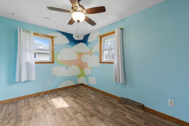 empty room with baseboards, visible vents, a ceiling fan, and wood finished floors