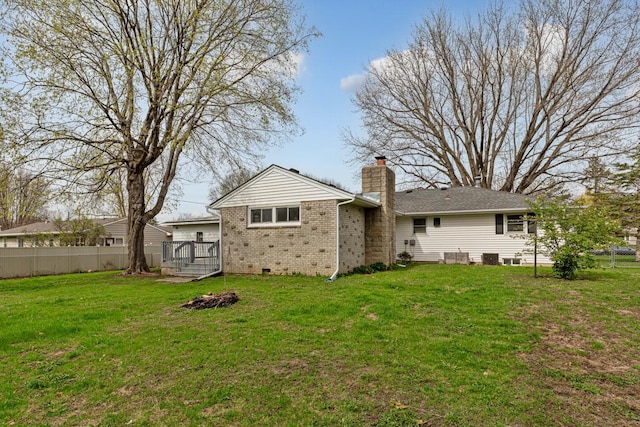 back of house featuring a chimney, brick siding, fence, and a lawn