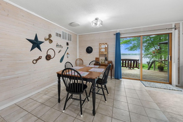 dining area featuring a textured ceiling, visible vents, wood walls, and light tile patterned floors