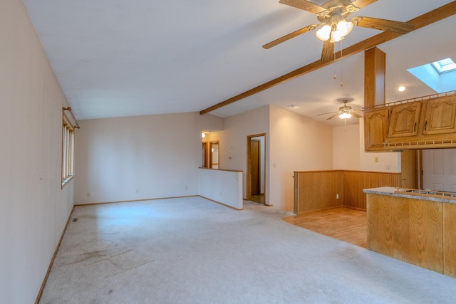 unfurnished living room with ceiling fan, light carpet, baseboards, and vaulted ceiling with skylight