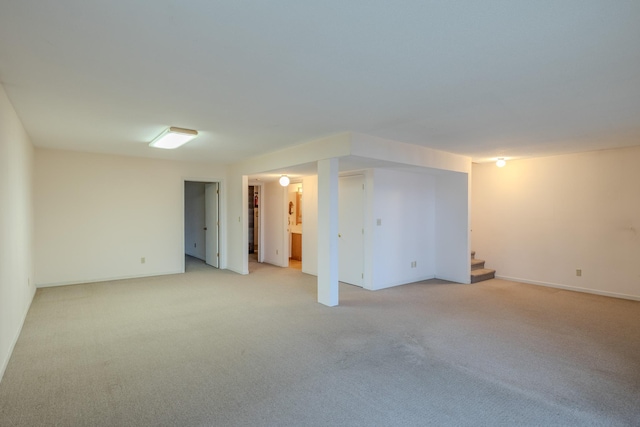 finished below grade area with baseboards, light carpet, and stairway