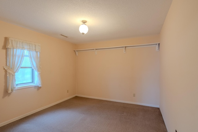 carpeted empty room with a textured ceiling, visible vents, and baseboards