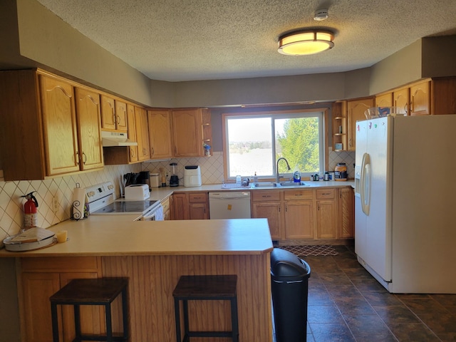 kitchen featuring under cabinet range hood, a sink, white appliances, a peninsula, and tasteful backsplash