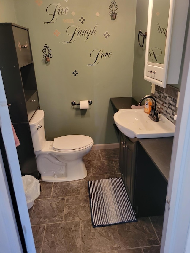 bathroom with toilet, decorative backsplash, vanity, baseboards, and stone finish floor