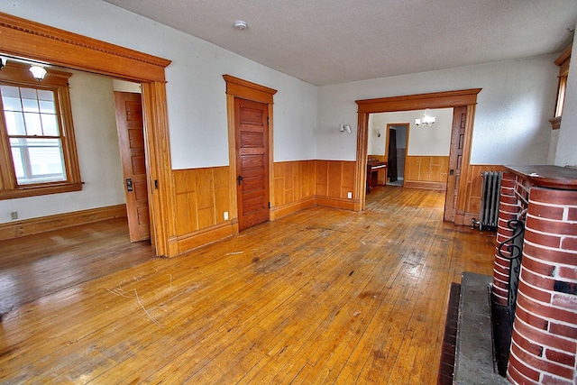 717 3rd St, Red Wing, MN 55066 - empty room featuring radiator heating unit, hardwood / wood-style floors, wooden walls, wainscoting, and a textured ceiling