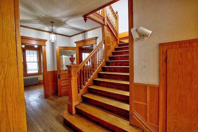 717 3rd St, Red Wing, MN 55066 - stairs featuring a wainscoted wall, a textured ceiling, radiator heating unit, crown molding, and hardwood / wood-style floors