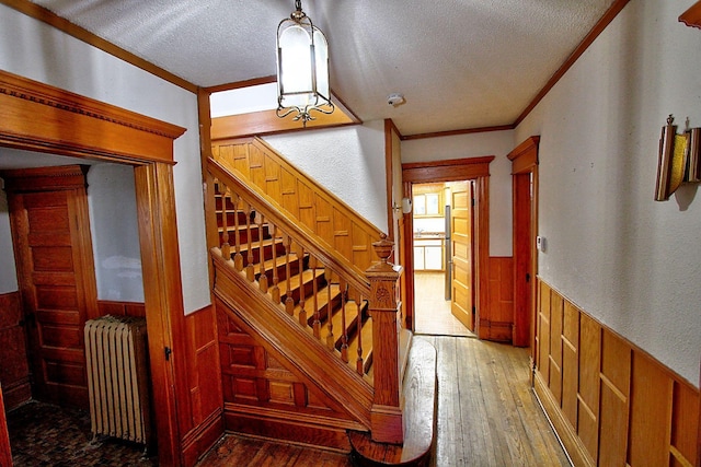 717 3rd St, Red Wing, MN 55066 - staircase with radiator, wood walls, ornamental molding, wainscoting, and a textured ceiling