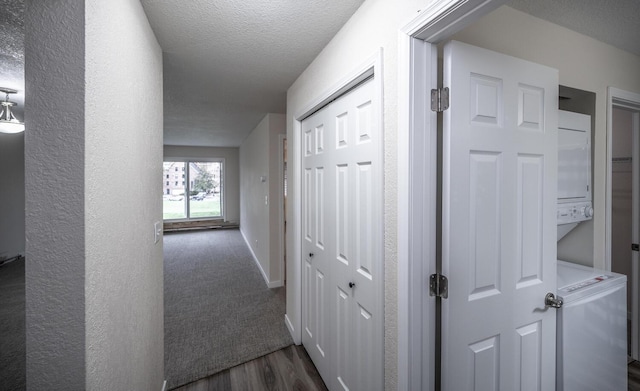 corridor featuring dark wood-style floors, stacked washer / drying machine, and a textured ceiling