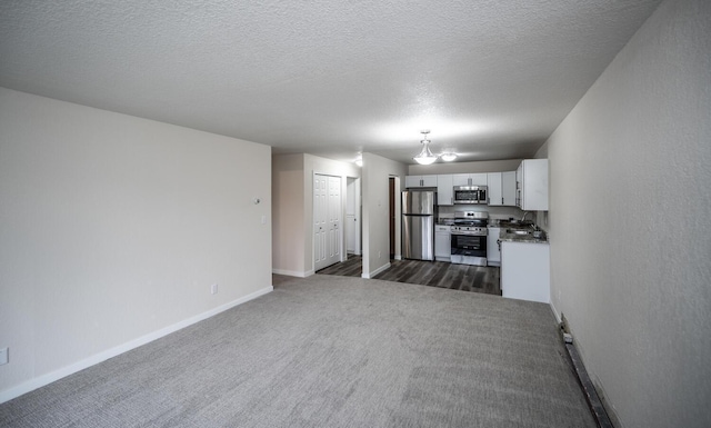 unfurnished living room with a textured ceiling, dark colored carpet, and baseboards