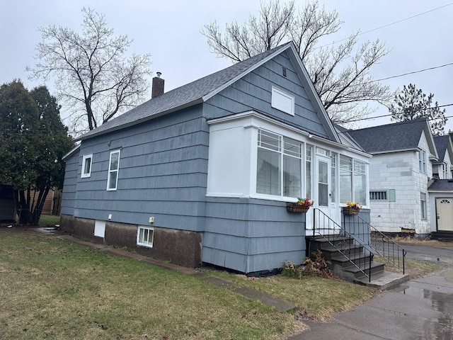 bungalow featuring a front lawn, roof with shingles, a chimney, and entry steps