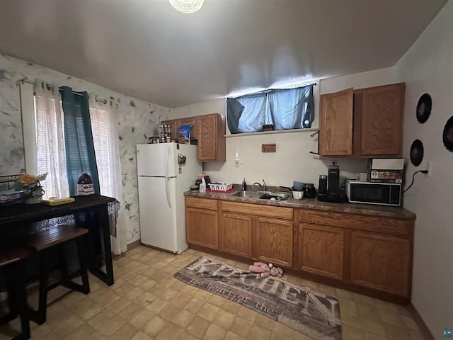 kitchen with a sink, freestanding refrigerator, black microwave, and dark countertops