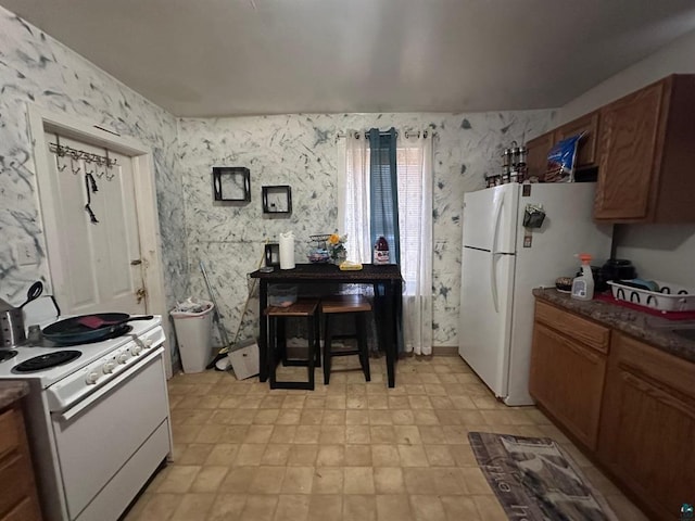 kitchen featuring brown cabinetry, white appliances, dark countertops, and wallpapered walls