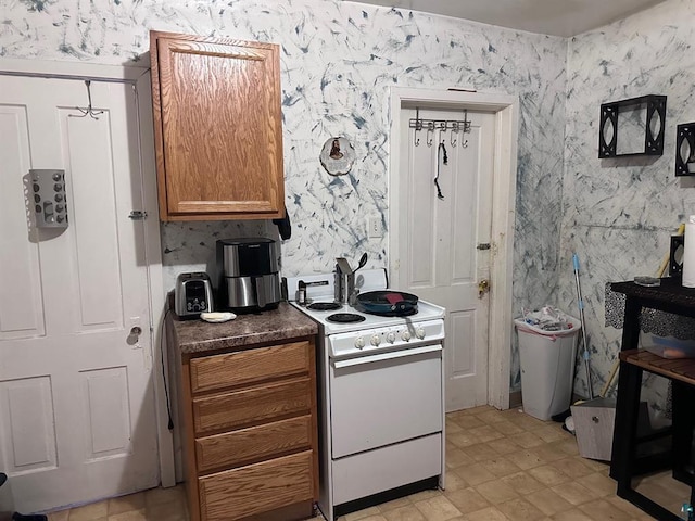 kitchen with wallpapered walls, dark countertops, brown cabinetry, and white range with electric cooktop