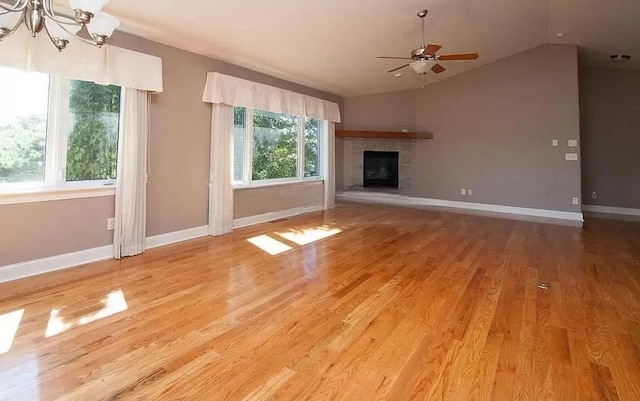 unfurnished living room featuring light wood-type flooring, a tiled fireplace, vaulted ceiling, baseboards, and ceiling fan with notable chandelier